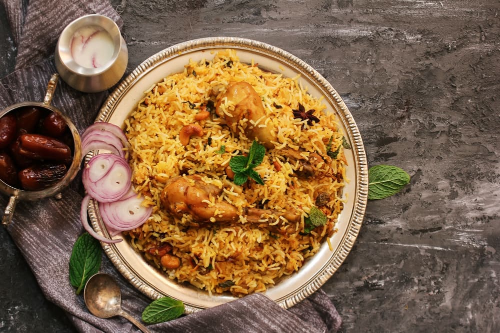 A platter of chicken biryani garnished with mint, with sliced onions and dates
