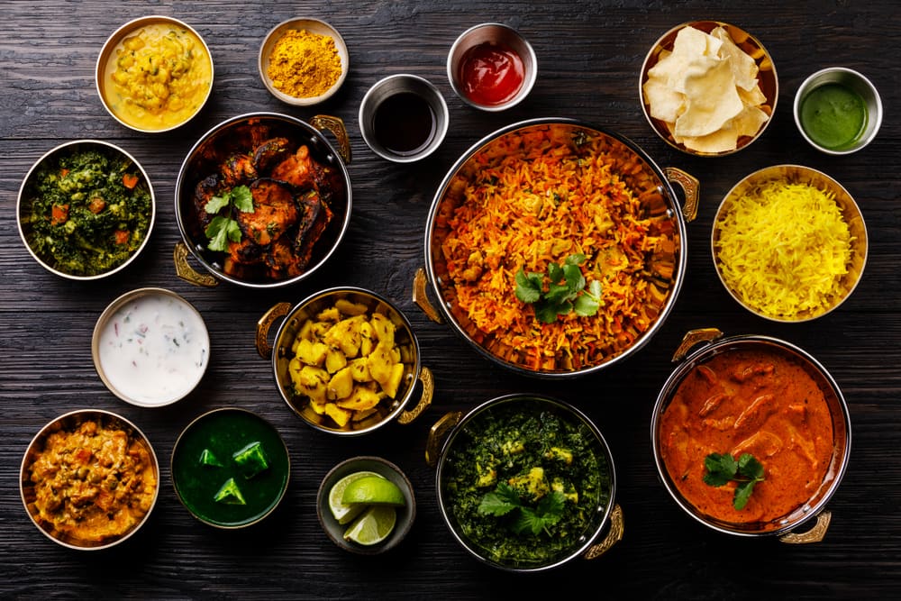 Overhead view of Indian dishes in copper bowls: biryani, curries, paneer, saag and rice