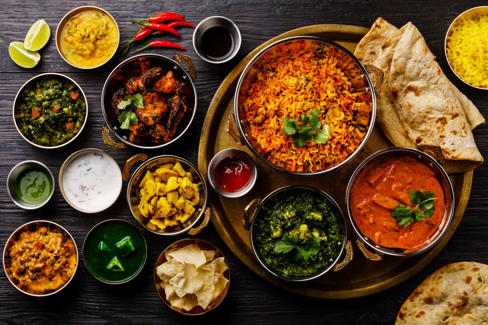 A brass tray of biryani and curries with naan, papad and chutneys