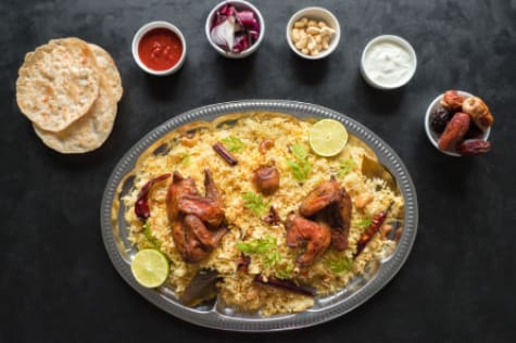 Chicken biryani on a dark platter with naan and small dishes